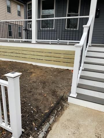Exterior view of a house with a porch, stairs, and newly built wooden retaining wall.