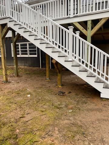 White staircase leading up to a deck. Black treads, wooden supports, and a grassy area.