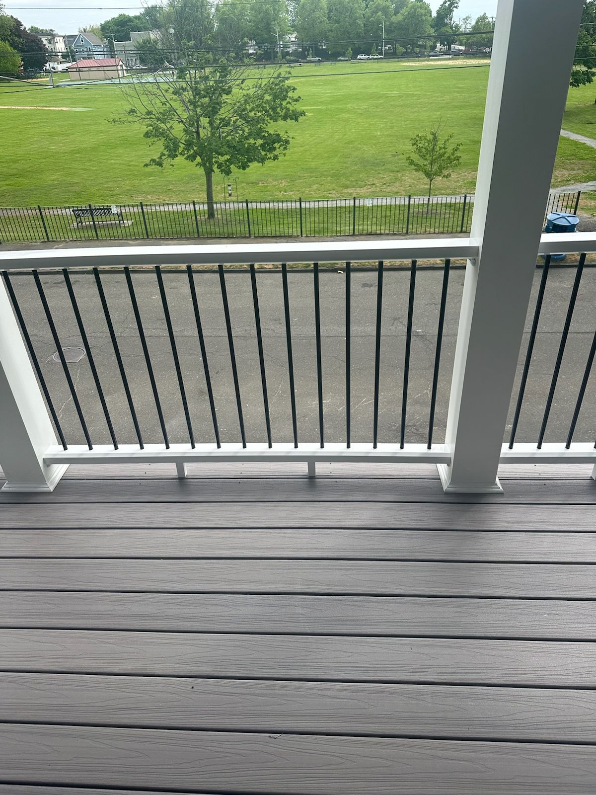 Deck with black railing overlooking a green field and street.