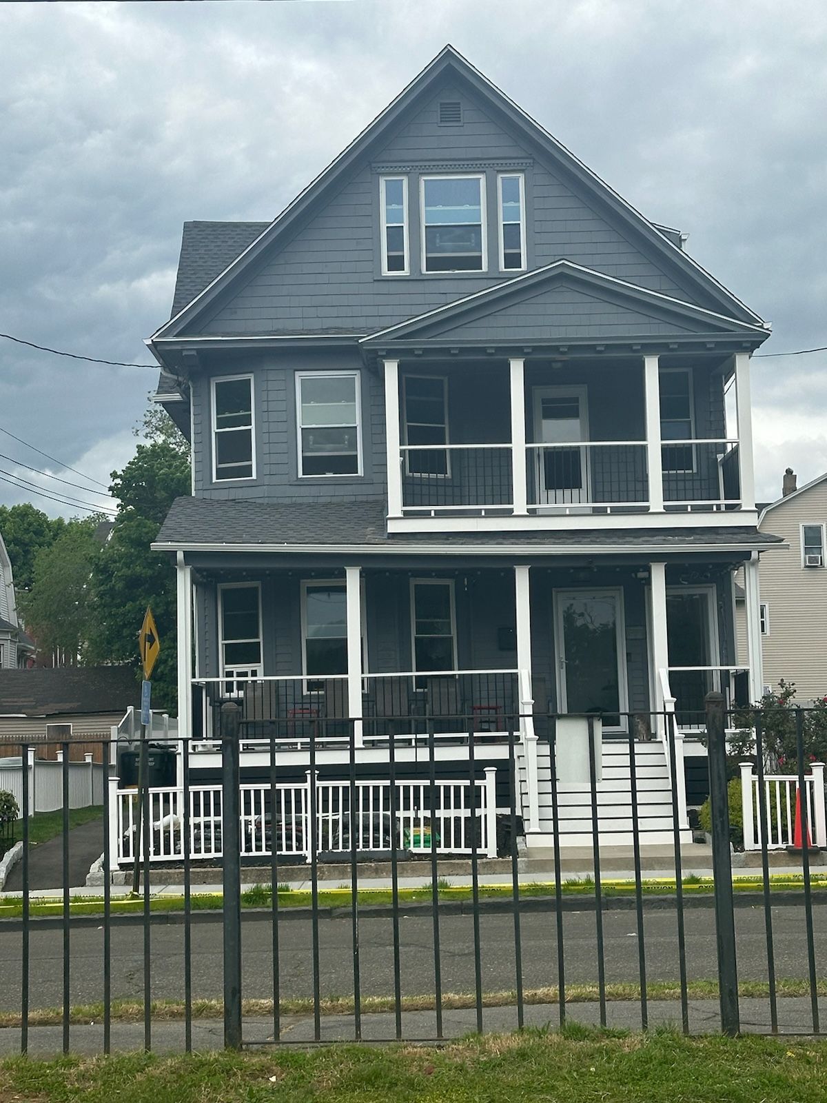 Gray three-story house with front porches. Black fence in front. Overcast day.