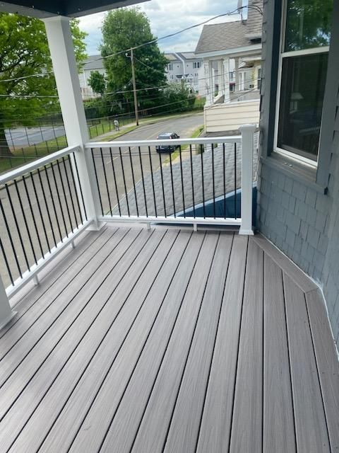 Gray composite deck with white railings and black vertical balusters on a porch overlooking a street.