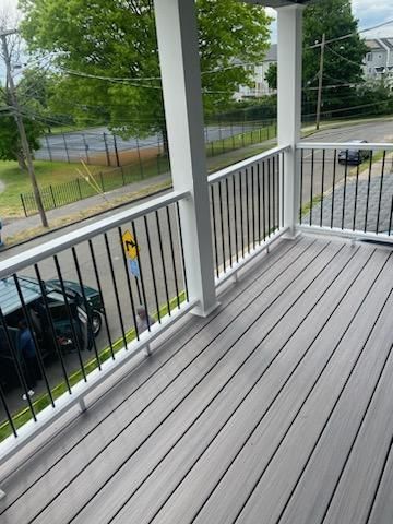 Gray deck with white railing and black spindles, overlooking a street and trees.