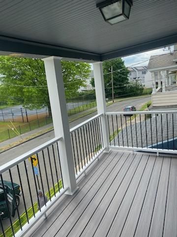 A gray composite deck on a porch with white columns and black railings overlooking a street.