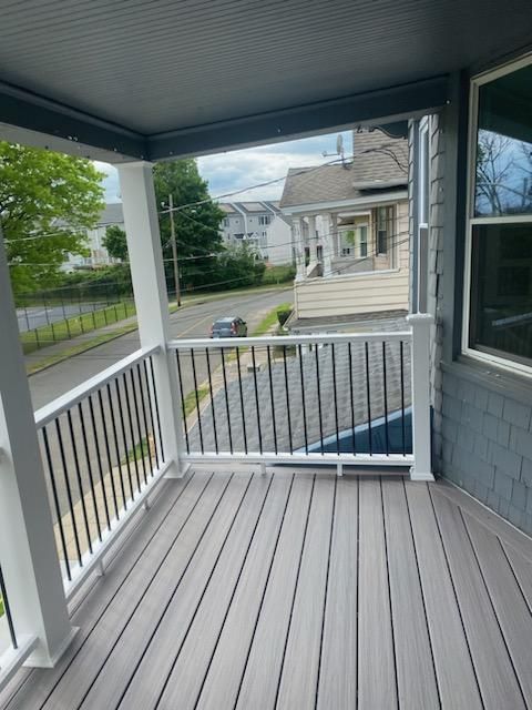 Covered porch with gray composite decking, white railing, and view of street.