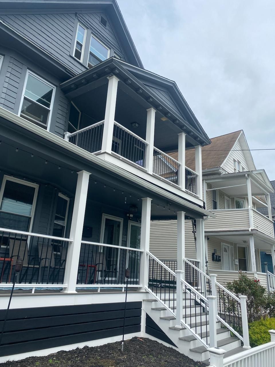 Two-story houses with porches and stairs; the one in front is gray with white trim.