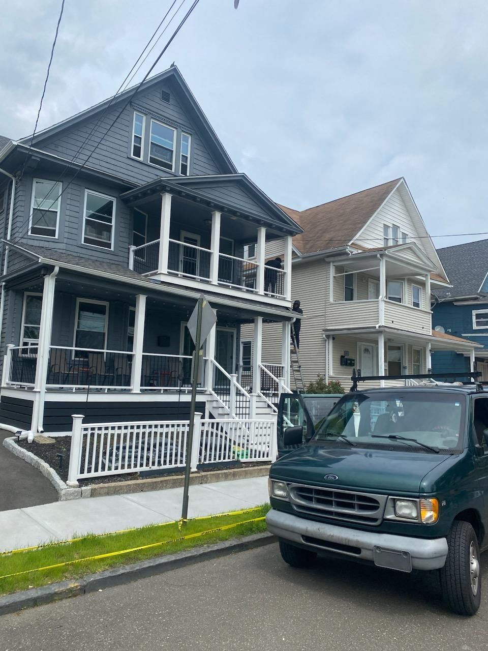 Two-story houses with porches and a green van parked on the street. Overcast sky.