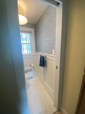 A narrow bathroom with white trim, blue accent wall, and patterned floor. A window lets in light.