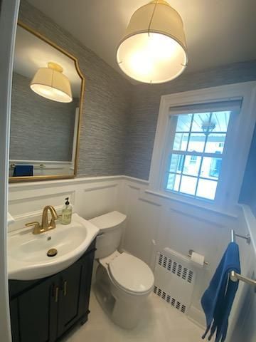 A small, stylish bathroom with a black vanity, gold fixtures, and a textured gray wall above white wainscoting.