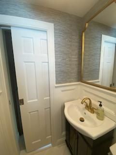 White bathroom with a sliding door, sink with gold faucet, and a large mirror.