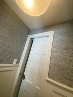 White door ajar in a room with gray textured wallpaper and white trim. Ceiling light.