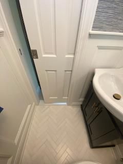 White bathroom with a door ajar, herringbone tile floor, and a dark cabinet with sink.