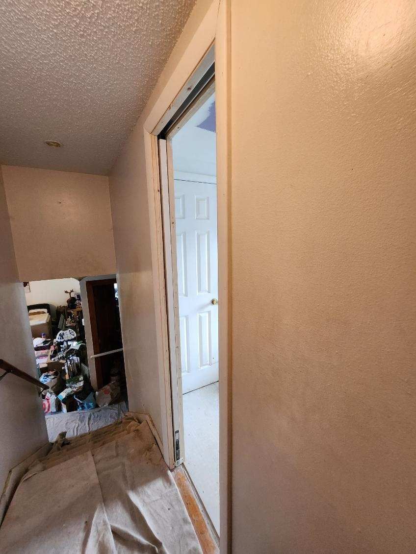 Hallway with open doorway, leading to a white door. The walls are a light color.