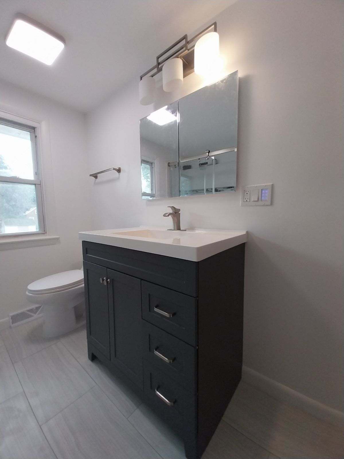 Bathroom with gray vanity, white countertop, mirror, light fixture, and toilet.