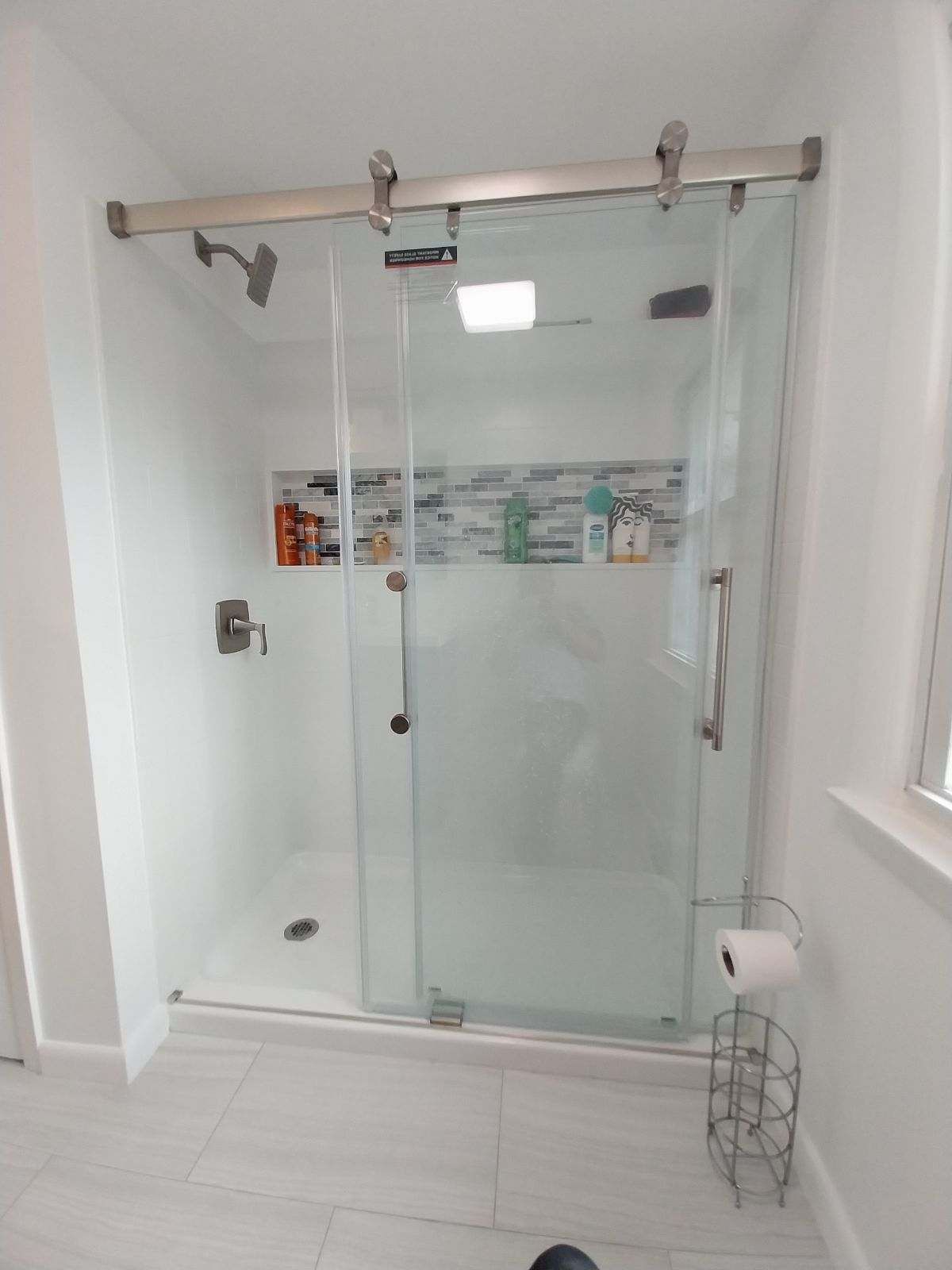 Glass shower with sliding door and silver hardware, in a white tiled bathroom.