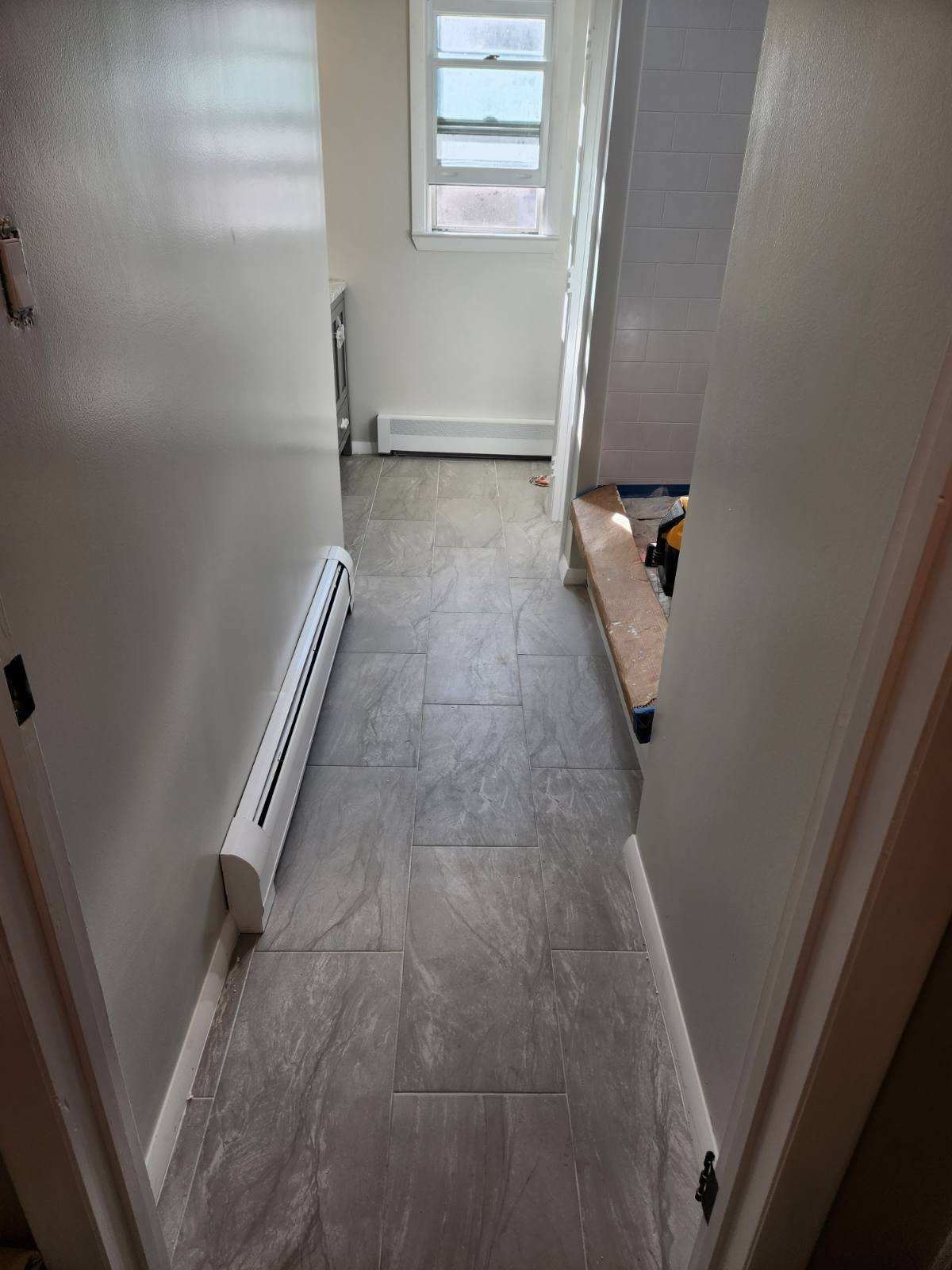 Narrow hallway with gray tile flooring, white walls, and a small window at the end.