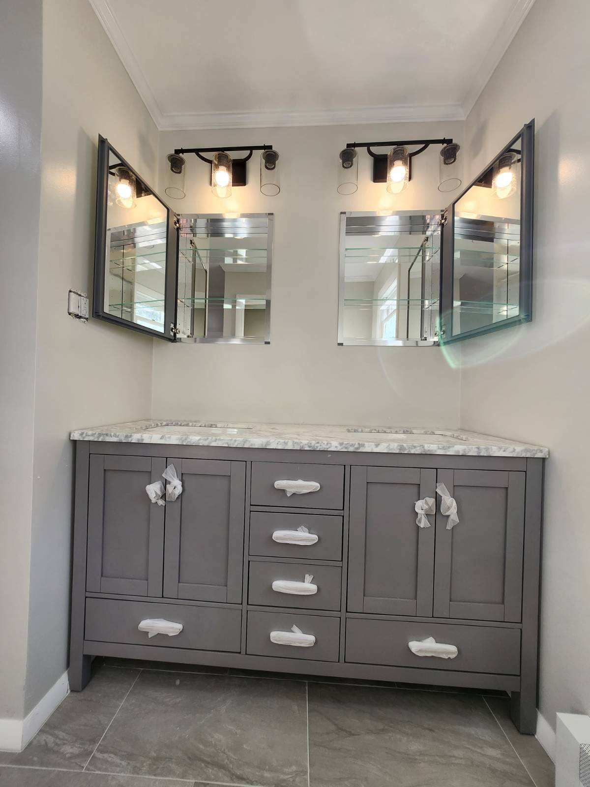 Gray vanity with marble countertop and two medicine cabinets in a bathroom.