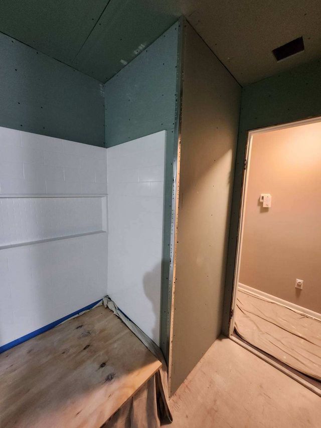 Corner of a bathroom under construction with white shower surround and green wall; door to the right.