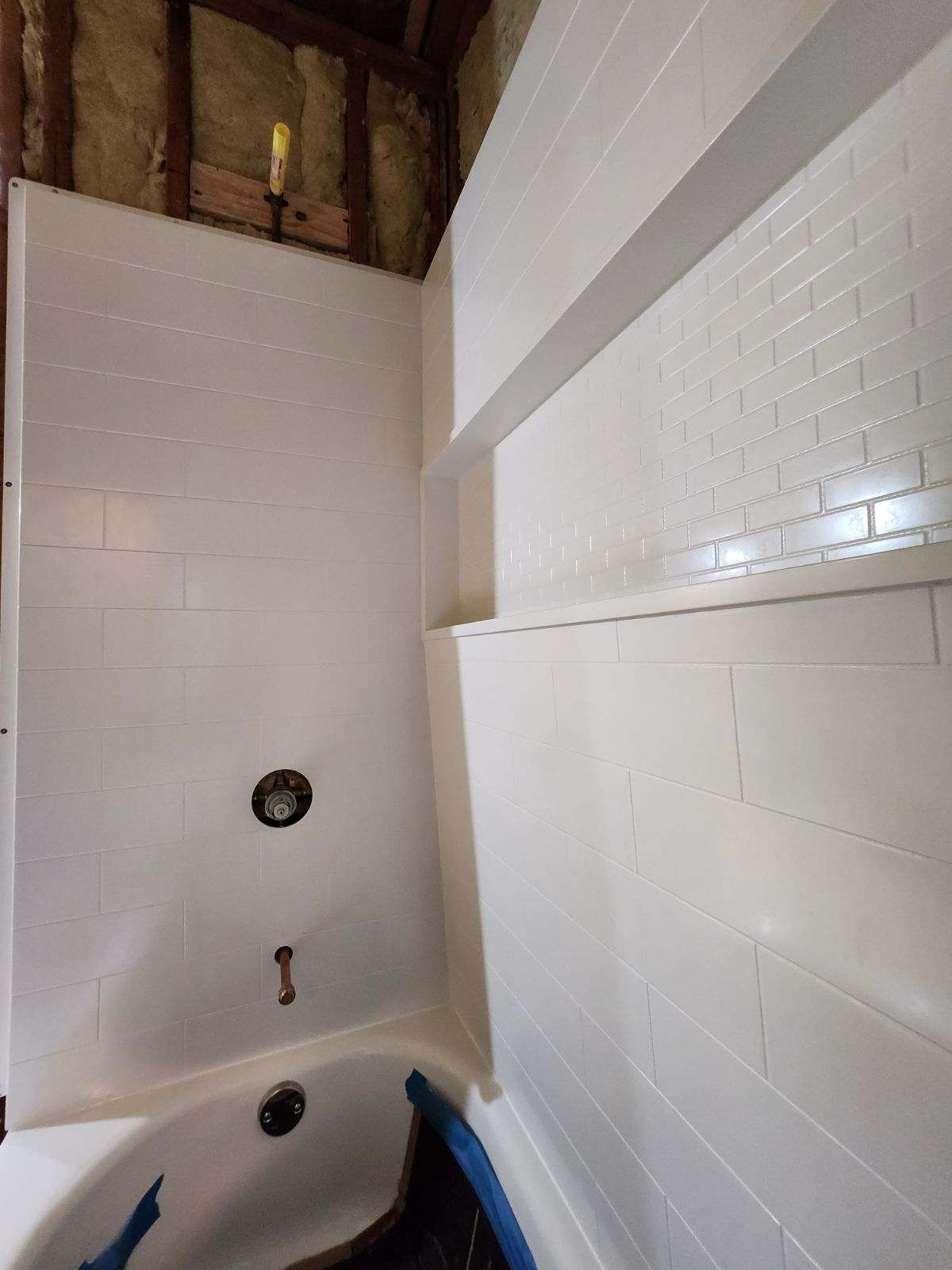 White-tiled bathroom with a bathtub, partially installed. Studs and insulation are exposed above.