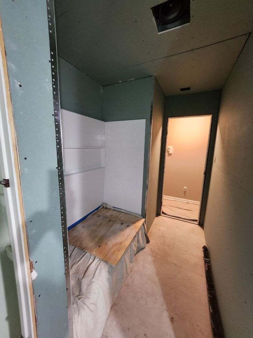 Interior view of a bathroom under construction, showing drywall, tile, and a hallway.
