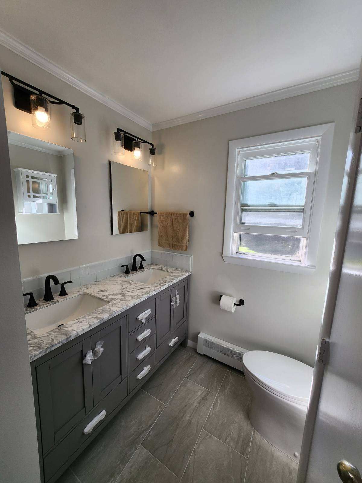 Bathroom with gray vanity, two sinks, black fixtures, and window.