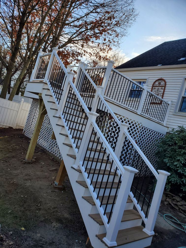 White deck with stairs, black latticework railings, leading to a house, outdoor setting.