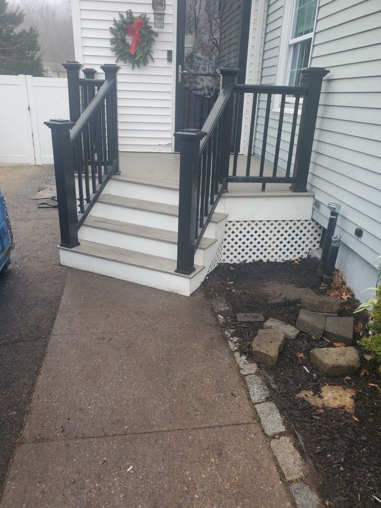 Black railing and steps leading up to a white house door with a wreath. Concrete walkway.