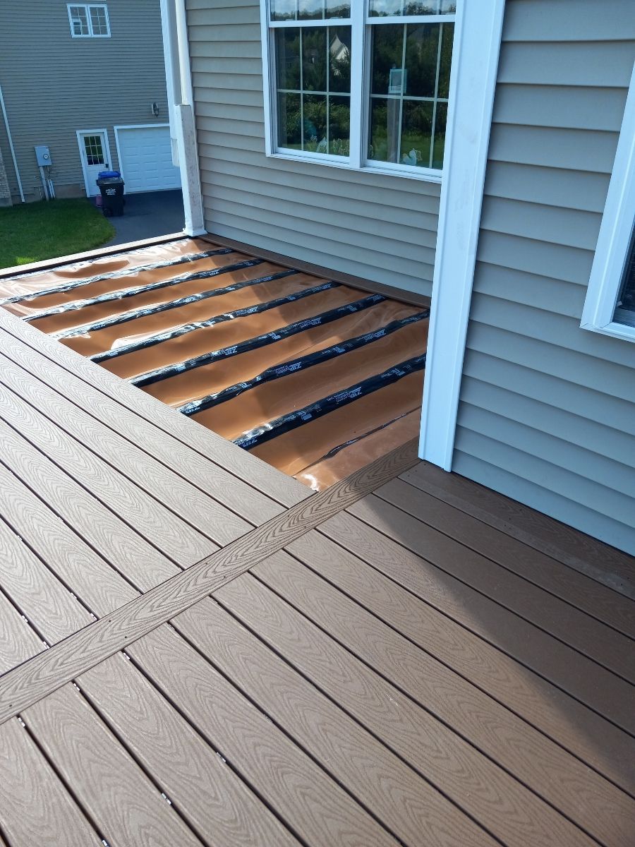 Partially constructed deck with brown composite boards; framing exposed. Sunlight. Building exterior.