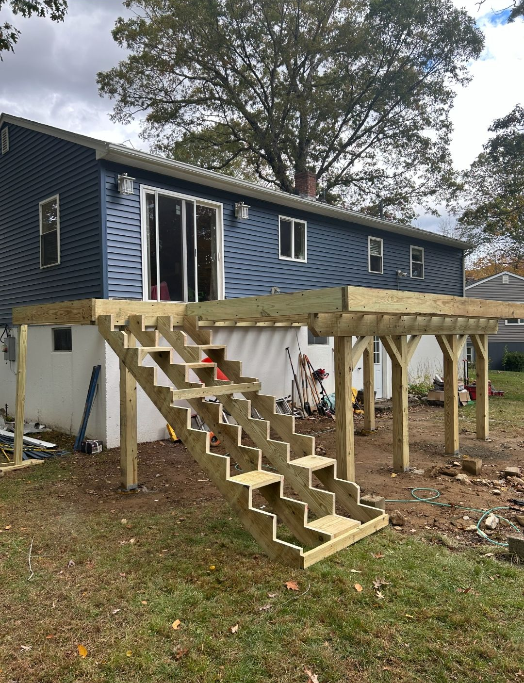 Wooden deck with stairs attached to a blue house in a yard.