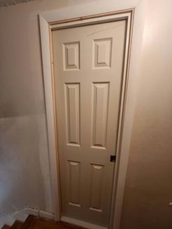 Beige six-panel door in a white frame, set in a hallway.