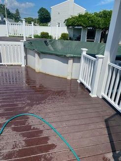 Wet wooden deck next to a partially covered above-ground pool with white railing on a sunny day.