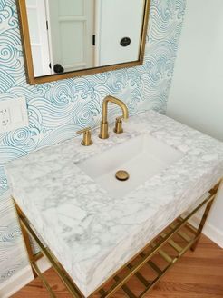 Marble countertop vanity with gold fixtures and wave-pattern wallpaper.
