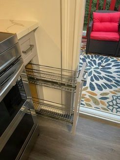 Pull-out kitchen cabinet with two wire shelves. Next to white cabinet door, and an open doorway.