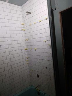 White subway tile partially installed in a shower, with yellow leveling spacers, and a turquoise tub visible.