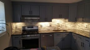 Gray kitchen cabinets with a tile backsplash and under-cabinet lighting.