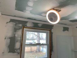Ceiling fan with a light ring installed on a ceiling being repaired; interior view with a window.