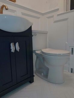 Navy blue bathroom vanity next to a white toilet in a white-walled bathroom.