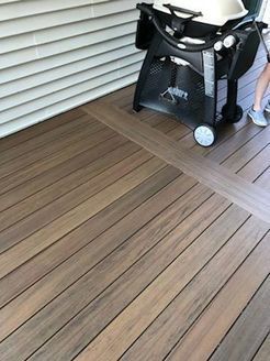 Composite deck with a grill and white siding.