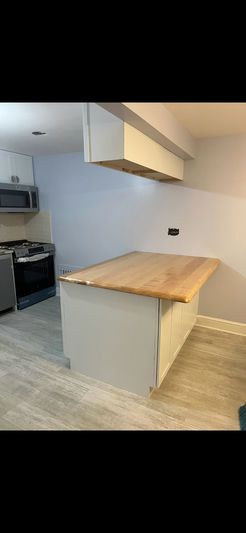 Kitchen with a light gray island and butcher block countertop, with a microwave and stove visible.