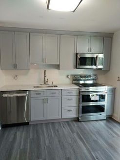Newly renovated kitchen with gray cabinets, stainless steel appliances, and gray flooring.
