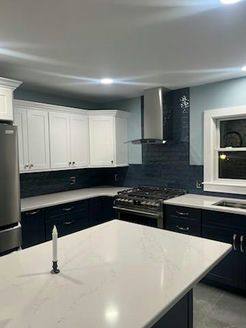Modern kitchen with white upper cabinets, navy blue lower cabinets, and stainless steel appliances.