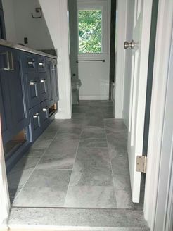 Bathroom hallway with blue cabinets, gray tile floor, and a door opening.
