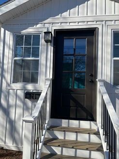 White house with black door, windows, and small porch steps.