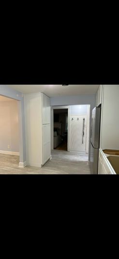 Kitchen interior with white cabinets, stainless steel fridge, and a hallway.