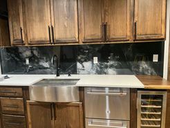 Kitchen with wooden cabinets, stainless steel sink and appliances, and a black and white backsplash.