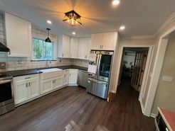 White kitchen with dark countertops and wood floors. Stainless steel appliances, bright lighting.