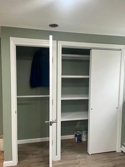 Two white-framed closets, one with a hanging jacket and the other with shelves. White sliding door open, room painted green.