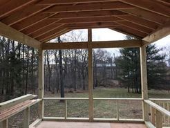 Screened-in porch under construction, overlooking a wooded yard.