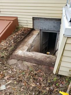Exterior basement entrance with concrete steps and door. Dirt and leaves surround the opening.