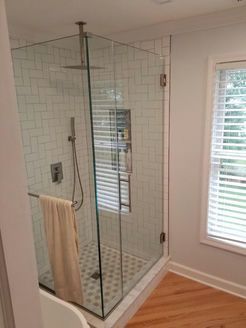 Glass-enclosed shower with white tiled walls and floor, stainless steel fixtures, and a towel hanging on the bar.