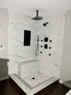 Modern shower with white marble-look tile, black fixtures, built-in seat, and a rectangular niche.